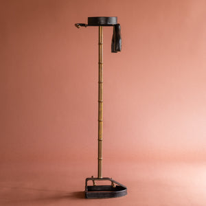 A side view of a 1950’s Valet de nuit; model 'Luxe' by Jacques Adnet, France. The vertical central tubular brass stand is made to look like bamboo. The base is leather in the shape of a horseshoe and it has a leather hanger at the top at an angle. 