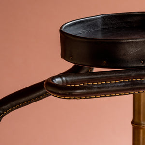 An angled close up view of a 1950’s Valet de nuit; model 'Luxe' by Jacques Adnet, France. Showing the vertical central tubular brass stand which is made to look like bamboo. A close up of the leather hanger and and oval leather tray at the top showing the leather covering and stitching.