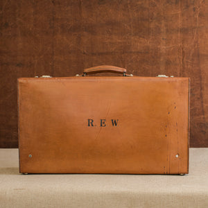Front view of the lid side of the leather case, circa 1925, handle at the top, just showing nickel plated brass locks at the top and the initials R.E.W. Brown and cream background.