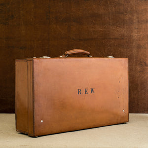 Front view of the lid side of the leather case, circa 1925, handle at the top, just showing nickel plated brass locks at the top and the initials R.E.W. Brown and cream background.