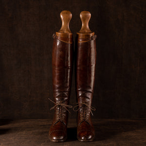 Front view of a pair of brown leather polo boots including their wooden trees made for Earl Spencer, Althorp Estate. They are laced up, side by side facing forwards on a brown background.