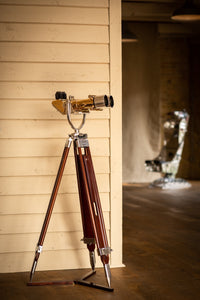Full length side view of Krauss of France brass and aluminium binoculars on a wood tripod with eye pieces on the left side with lens on the right side. White and dark wood background.