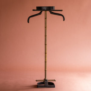A front view of a 1950’s Valet de nuit; model 'Luxe' by Jacques Adnet, France. The vertical central tubular brass stand is made to look like bamboo. The base is leather in the shape of a horseshoe and it has a leather hanger at the top at an angle. 