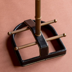 A close up view of a 1950’s Valet de nuit; model 'Luxe' by Jacques Adnet, France. Showing the vertical central tubular brass stand which is made to look like bamboo and the base which has two horizontal brass bars crossing a horseshoe shaped leather covered and stitched base.