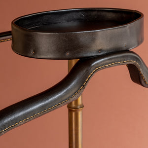 A close up view of a 1950’s Valet de nuit; model 'Luxe' by Jacques Adnet, France. Showing the vertical central tubular brass stand which is made to look like bamboo. A close up of the leather hanger and and oval leather tray at the top for cufflinks, keys, coins, etc at a slight angle angle. 