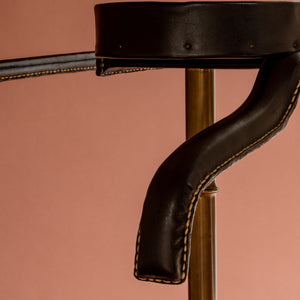 A close up view of a 1950’s Valet de nuit; model 'Luxe' by Jacques Adnet, France. Showing the vertical central tubular brass stand which is made to look like bamboo. A close up of the leather hanger and and oval leather tray at the top showing the leather covering and stitching.