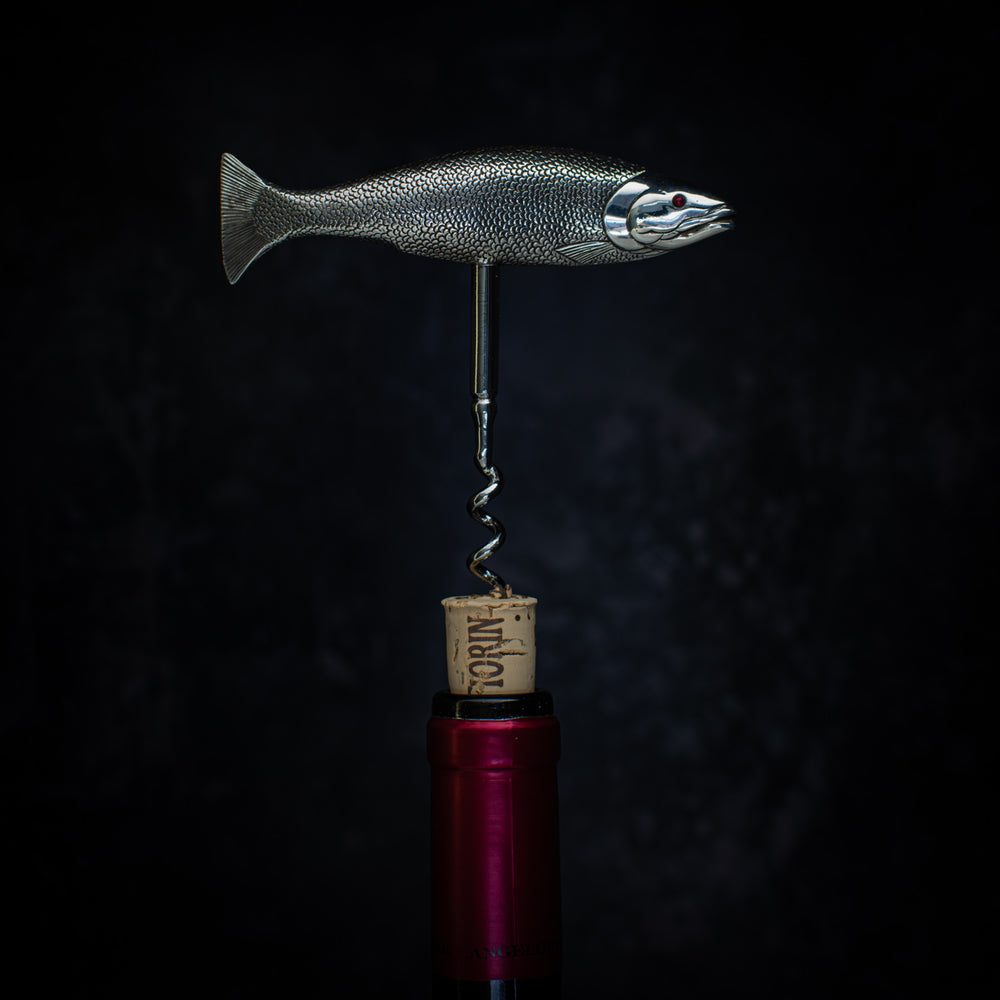 Side view of a corkscrew pulling a cork from a wine bottle. The handle is in the form of a salmon with the tail on the left and the head on the right. Cast in silver and beautifully detailed, showing the mouth, fins and even the scales. The fish is modelled as if 'on the move' so it sits in the hand very comfortably when the corkscrew is in use. 