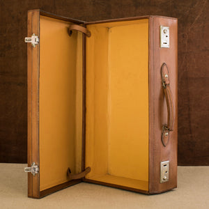 Sitting open on it’s side showing the yellow Rexine lining inside of the leather case, on the right side showing the handle and nickel plated brass locks, circa 1925. Brown and cream background.