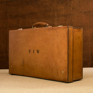 View at a diagonal angle of the lid side of the leather case, circa 1925, handle at the top, just showing nickel plated brass locks at the top and the initials  F.I.W. Brown and cream background.