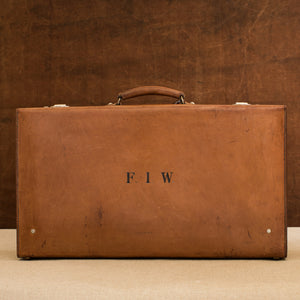View of the lid side of the leather case, circa 1925, handle at the top, just showing nickel plated brass locks at the top and the initials F.I.W.  Brown and cream background.