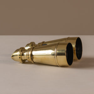 View of a pair of polished brass hand held binoculars by L. Petit of Paris, France, circa 1905, lying horizontally on their side. The eye pieces are on the left of the photo, you can just see the lenses on the right side.