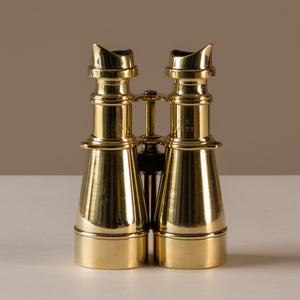 Rear view of a pair of polished brass hand held binoculars by L. Petit of Paris, France, circa 1905. The eye pieces are at the top of the photo, sitting upright. Showing the stamped  British ordinance broad arrow mark, serial no. and 'S.3' (grade marking used in WWI for the type and quality of the binocular; in this case 'high-grade Galilean').