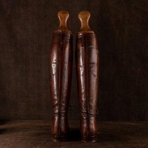 Rear view of a pair of brown leather polo boots including their wooden trees, made for Earl Spencer, Althorp Estate. Rear of boots showing, placed side by side on a brown background.