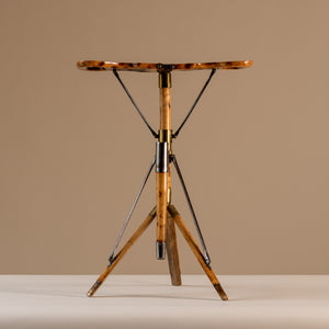 The image shows an Edwardian shooting stick seat forming a three legged stool in beech wood, brass and steel, circa 1910. The stool sits central on a beige and cream background with tripod legs splayed and the seat opened facing forwards.