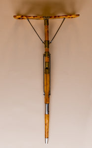 The image is from above, it shows an Edwardian shooting stick with the tripod base in the steel and beech wood cover turning it into a shooting stick seat. The seat at the top is opened into a seat. All made of beech wood, brass and steel, circa 1910. They are against a beige and cream background.