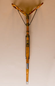 The image is from above, it shows an Edwardian shooting stick with the tripod base in the steel and beech wood cover turning it into a shooting stick seat. The seat at the top is midst opening into a seat. All made of beech wood, brass and steel, circa 1910. They are against a beige and cream background.