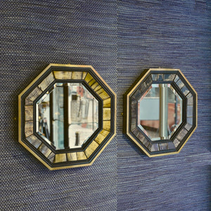 Front view of a side by side pair of 1970’s Antony Redmile octagonal brass framed bevelled glass mirrors with inset horn and ebonised wood surround with a blue woven background.