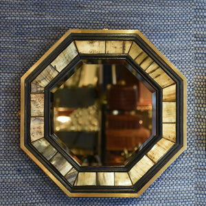 Front view of 1970’s Antony Redmile octagonal brass framed bevelled glass mirror with inset horn and ebonised wood surround with a blue woven background.