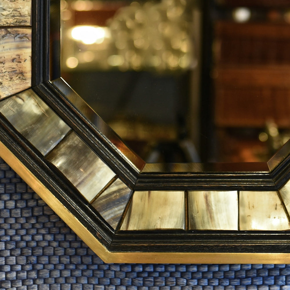 Detail of part of 1970’s Antony Redmile octagonal brass framed bevelled glass mirror with inset horn and ebonised wood surround with a blue woven background.