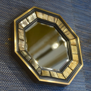 View from a diagonal of the below left side and front of a 1970’s Antony Redmile octagonal brass framed bevelled glass mirror with inset horn and ebonised wood surround with a blue woven background.
