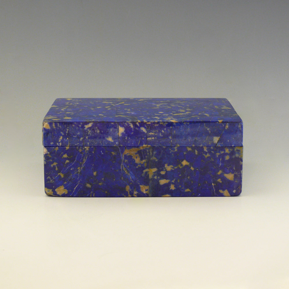 Front view of a box made from Lapis Lazuli with a cobalt blue base colour and beige and dark blue mottling running through the stone. Makers mark for George Betjemann and Sons, 1928. White background.