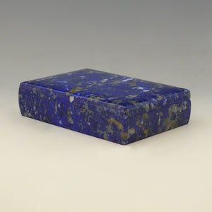 A front view from an angle with the front right corner in the foreground of a Lapis Lazuli box with a cobalt blue base colour and white, beige and dark blue mottling running through the stone. white background.