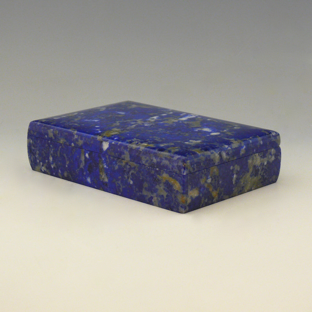A front view from an angle with the front right corner in the foreground of a Lapis Lazuli box with a cobalt blue base colour and white, beige and dark blue mottling running through the stone. white background.