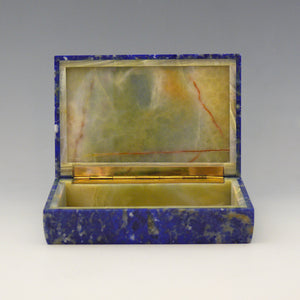 A front view of an open stone box with a yellow stone inside and gilt hinge along the edge adjoining the lid. The outside of the box is Lapis Lazuli with a cobalt blue base colour and white, beige and dark blue mottling running through the stone. white background.